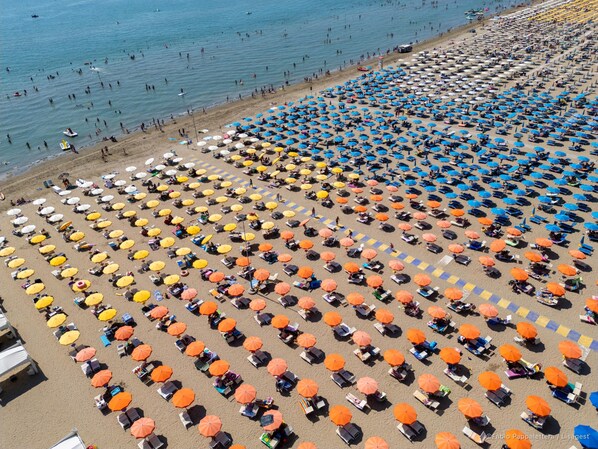 Ein Strand mit Reihen von Sonnenschirmen und Liegestühlen, freier Blick auf das Meer und Menschen beim Schwimmen.