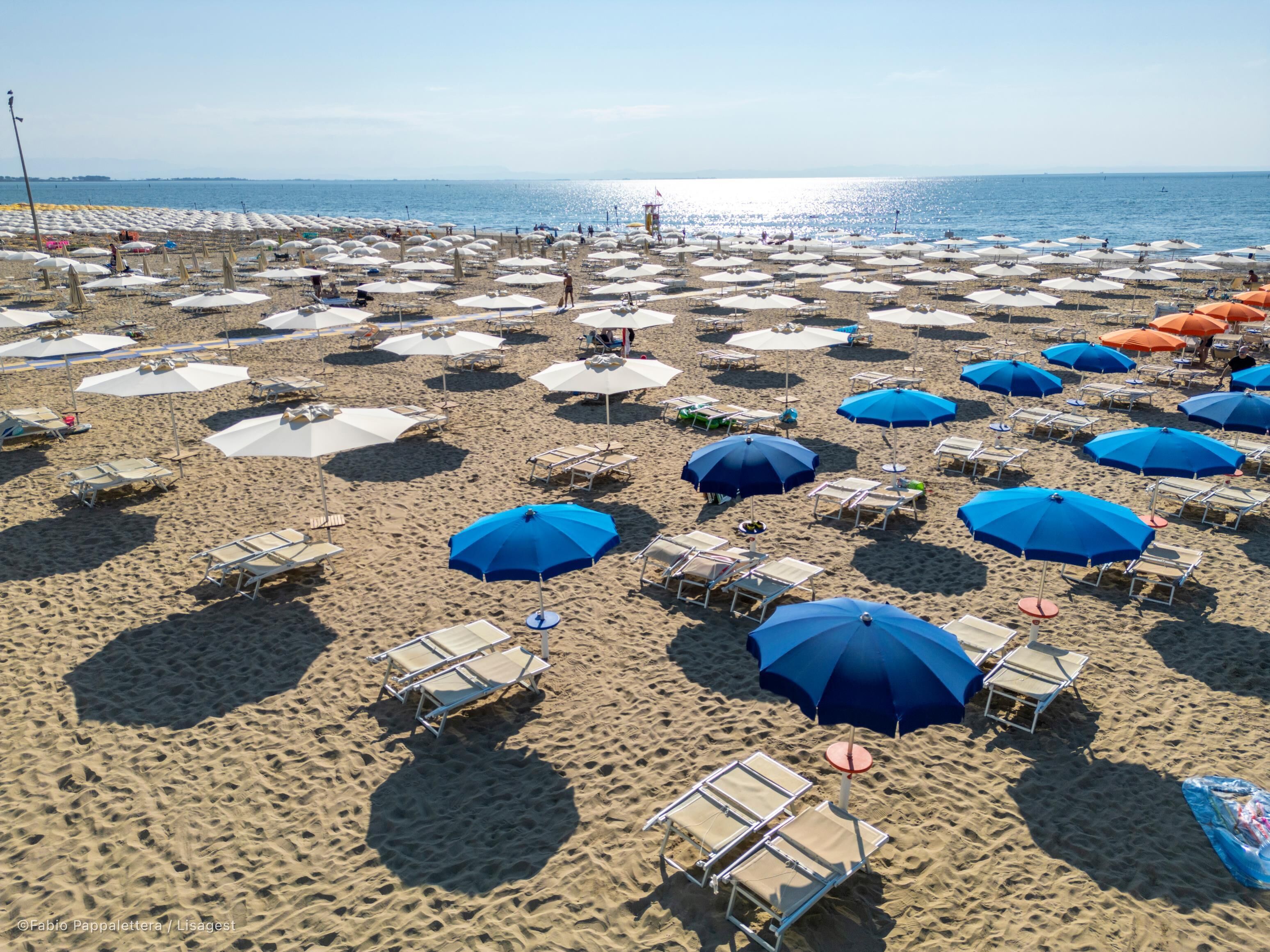 Een strand met tal van parasols en ligbedden, netjes op rijen gerangschikt.