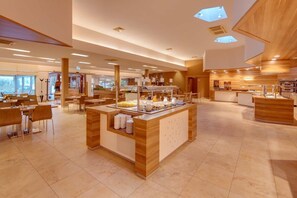 Un hall d’hôtel moderne doté d’un espace buffet central, de différents types de sièges et d’une grande fenêtre offrant une vue sur l’extérieur.
