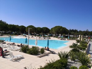 Un espace piscine doté de plusieurs chaises longues et de parasols, entouré de verdure et d’arbres.