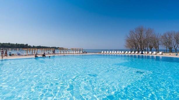 Une grande piscine d’un bleu éclatant, dotée de chaises longues et d’une pergola en bois.