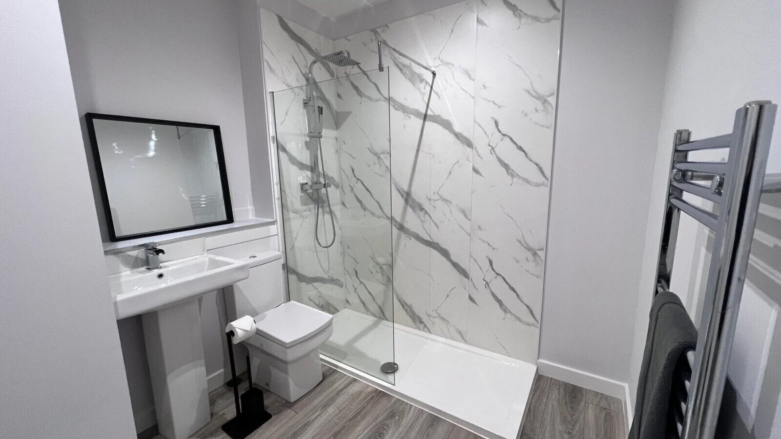Un bany modern amb paret de dutxa de marbre, un vàter, un lavabo i un mirall.