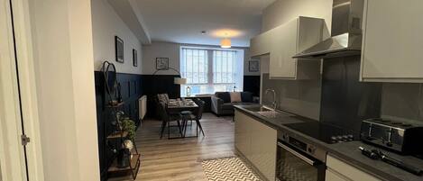Una cocina moderna con horno integrado, estufa y pileta. Hay un comedor con una mesa y sillas, y un ventanal que proporciona luz natural.