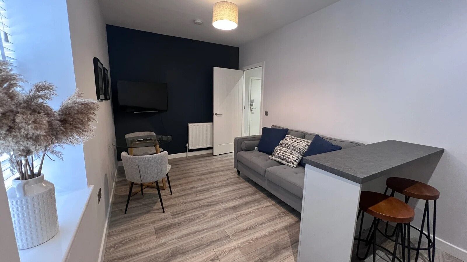 En moderne stue med en grå sofa, et glasbord og en bar med barstole.
