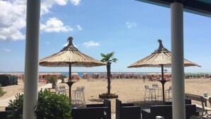 Eine Terrasse am Strand mit Reetdachschirmen, Sitzgelegenheiten im Freien und Blick auf den Strand.