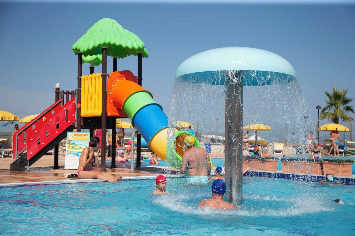 Un parc aquatique doté d’un grand toboggan aquatique, d’une piscine et d’un espace couvert avec des parasols.