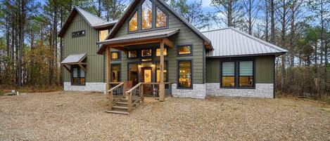 A two-story log cabin with a stone foundation, large windows, and a covered front porch.