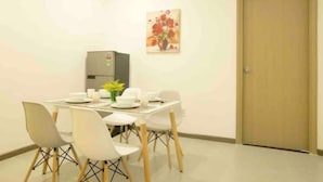 A dining area with a table set for four, white chairs, a refrigerator, and a painting on the wall.