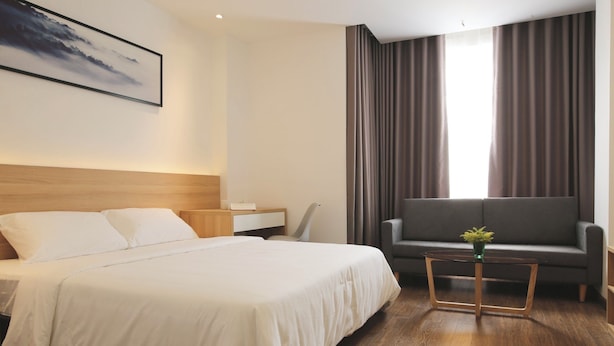 A hotel room with a large bed, a sofa, a small table with a plant, and a painting on the wall.