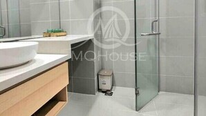 A modern bathroom with a glass shower enclosure, a white sink, and a small trash bin.