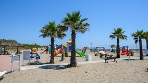 Une aire de jeux de plage avec différentes structures ludiques, des palmiers et un ciel dégagé.