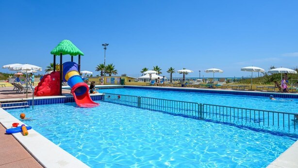 Une piscine avec un toboggan, des parasols et des chaises longues.