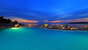 A pool with lounge chairs and a sunset view.