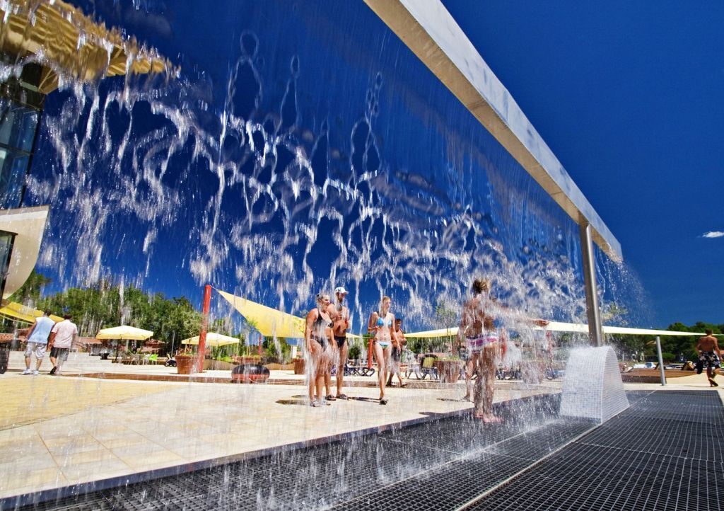 Ein Wasserspiel mit mehreren Düsen, einem gefliesten Boden und blauem Himmel.