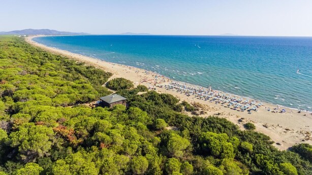 Vista aérea de una playa con vegetación densa en un lado y una playa arenosa con sombrillas y gente en el otro.