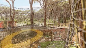 Un puente colgante sobre una estructura de malla con árboles al fondo.