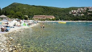Une plage avec une eau claire et peu profonde, un hôtel en arrière-plan et un paysage vallonné.