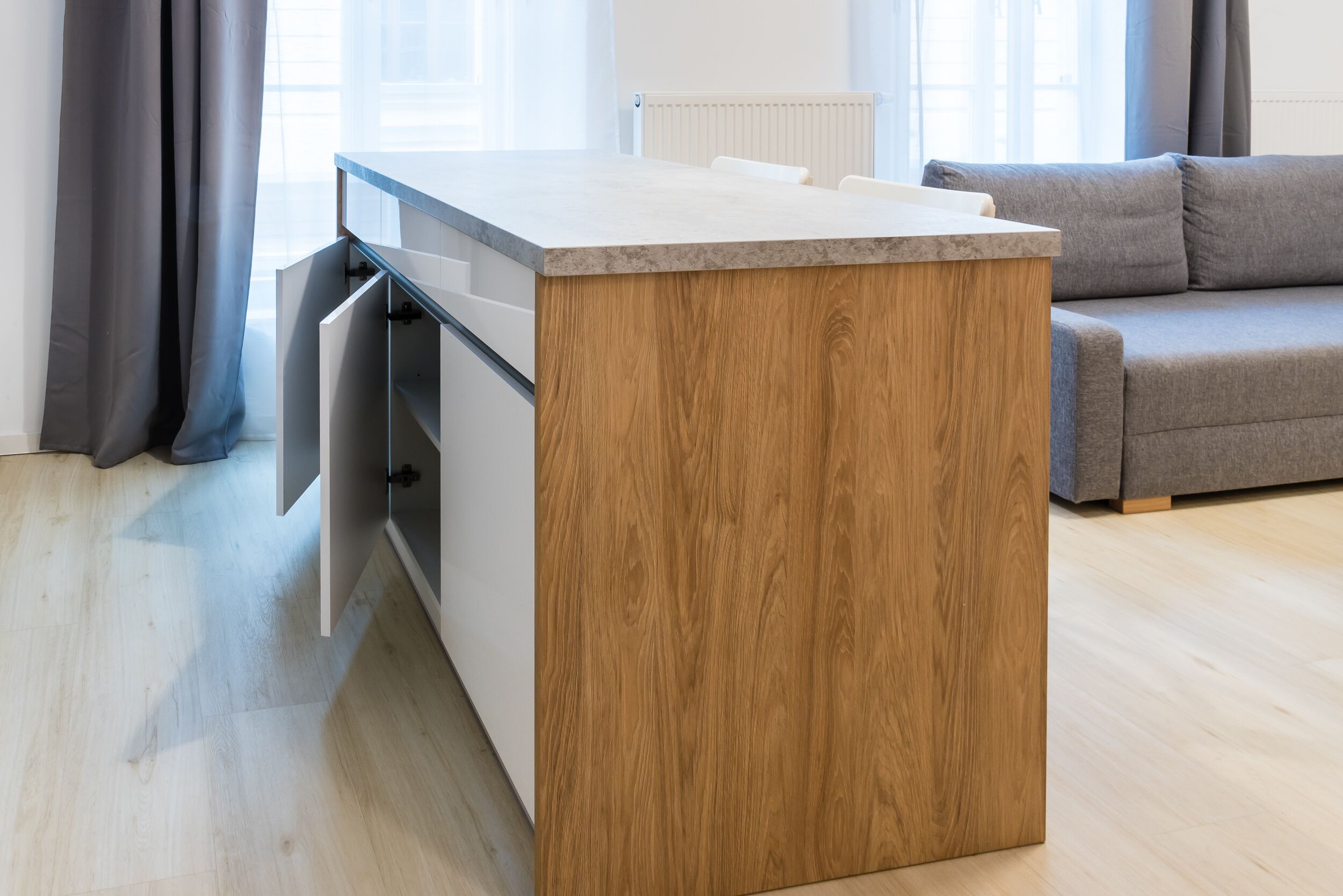 A modern kitchen with a wooden accent wall, a built-in oven, and a grey sofa in the living area.