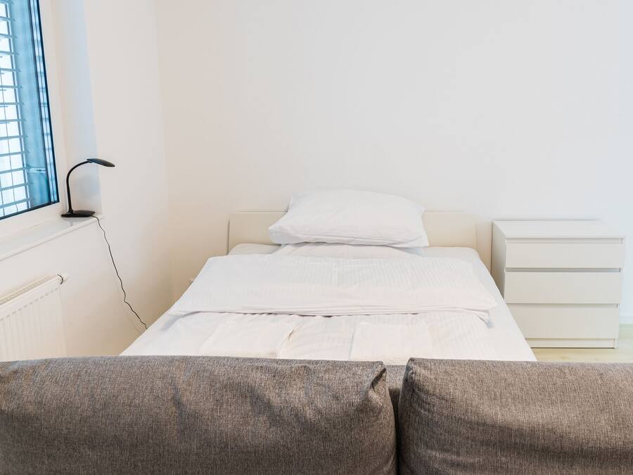 A bedroom with a bed, a bedside table, a lamp, and a window with blinds.