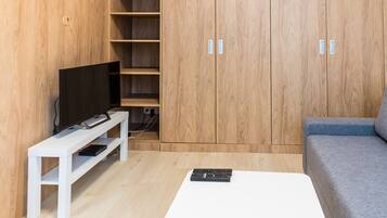 A modern living room with a flat-screen TV on a white stand, a grey sofa, and a wooden wardrobe with two doors.