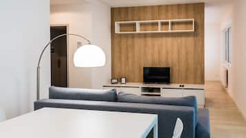 Ein modernes Wohnzimmer mit einem grauen Sofa, einem weißen Tisch, einem Fernseher an einer Holzwand und einer Stehlampe.