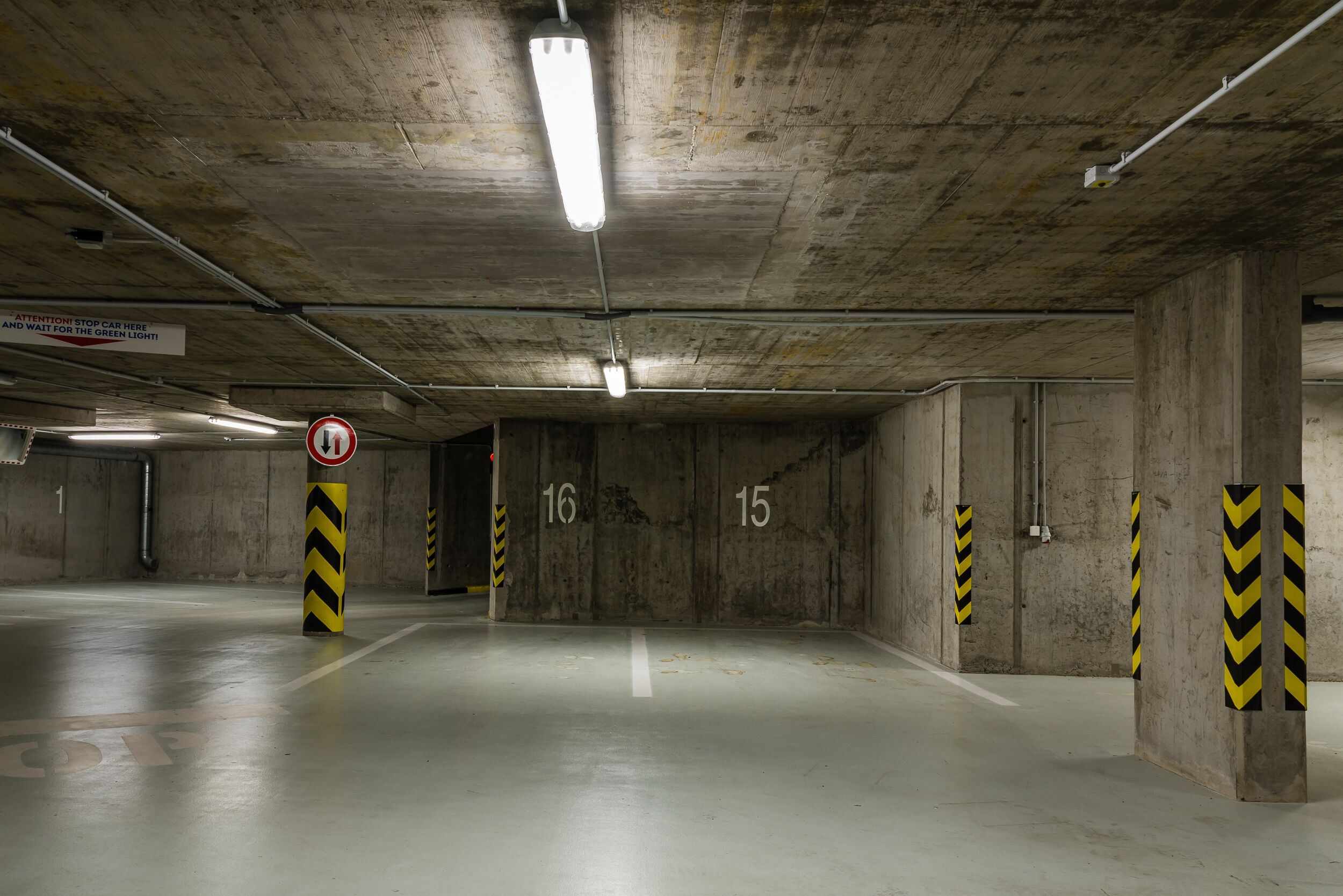 An underground parking garage with concrete walls, numbered parking spots, and caution signs.