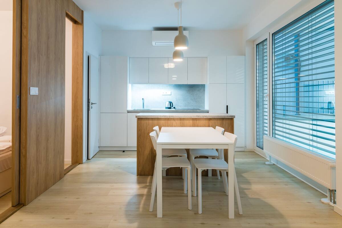Una cocina moderna con armarios blancos, encimera de madera y un comedor con mesa y sillas blancas.