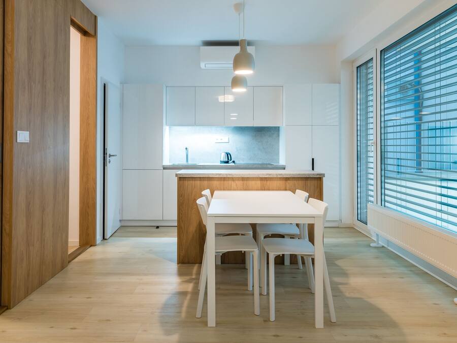 A modern kitchen with white cabinets, a wooden countertop, and a dining area with a white table and chairs.