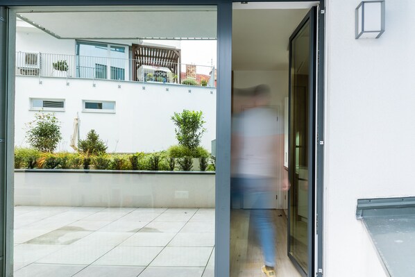Een modern gebouw met een glazen deur die uitkomt op een binnenplaats met betegelde vloeren en potplanten.
