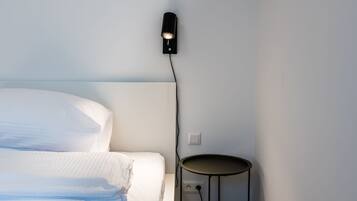 Un lit bien fait, avec du linge de lit blanc, une petite table ronde et un luminaire fixé au mur.