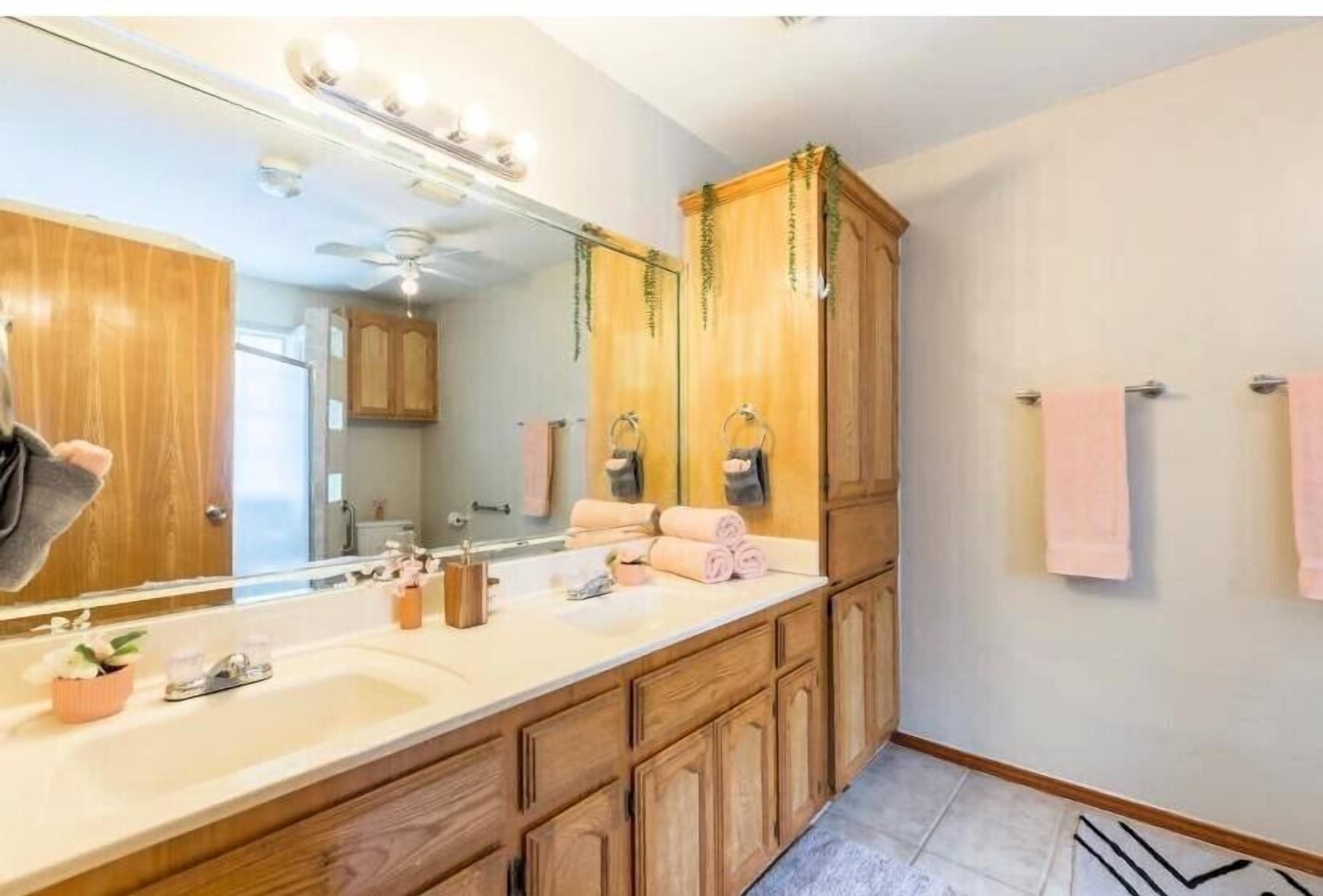 A bathroom with wooden cabinets, a large mirror, and a vanity with a sink.