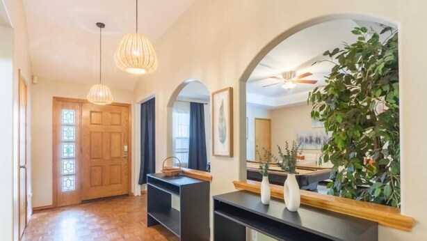 A hallway with wooden flooring, a wooden door with glass panels, black shelving units, and a mirror reflecting a plant and a ceiling fan. - McAllen Majesty 4BR w Pool and Comfort (McAllen)