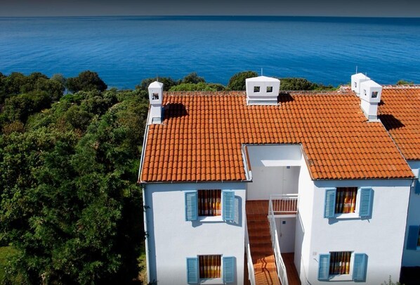 Um edifício de dois andares com telhado de telhas vermelhas, paredes brancas e persianas azuis.