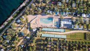 An aerial view of a coastal area with a large swimming pool, several RVs, and a mix of residential and commercial buildings.