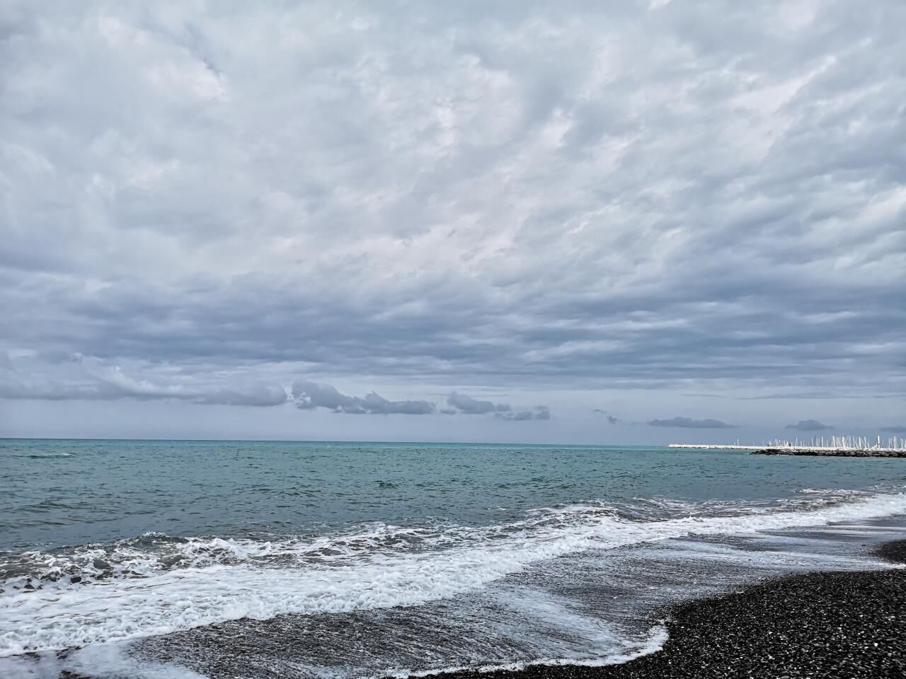 A beach with waves, a cloudy sky, and a distant pier.
