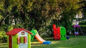 Ein Kinderspielbereich mit einem kleinen Haus, Rutschen und einer Schaukel.