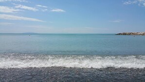 Ein Strand mit ruhigem Wasser, einer felsigen Küste und blauem Himmel.