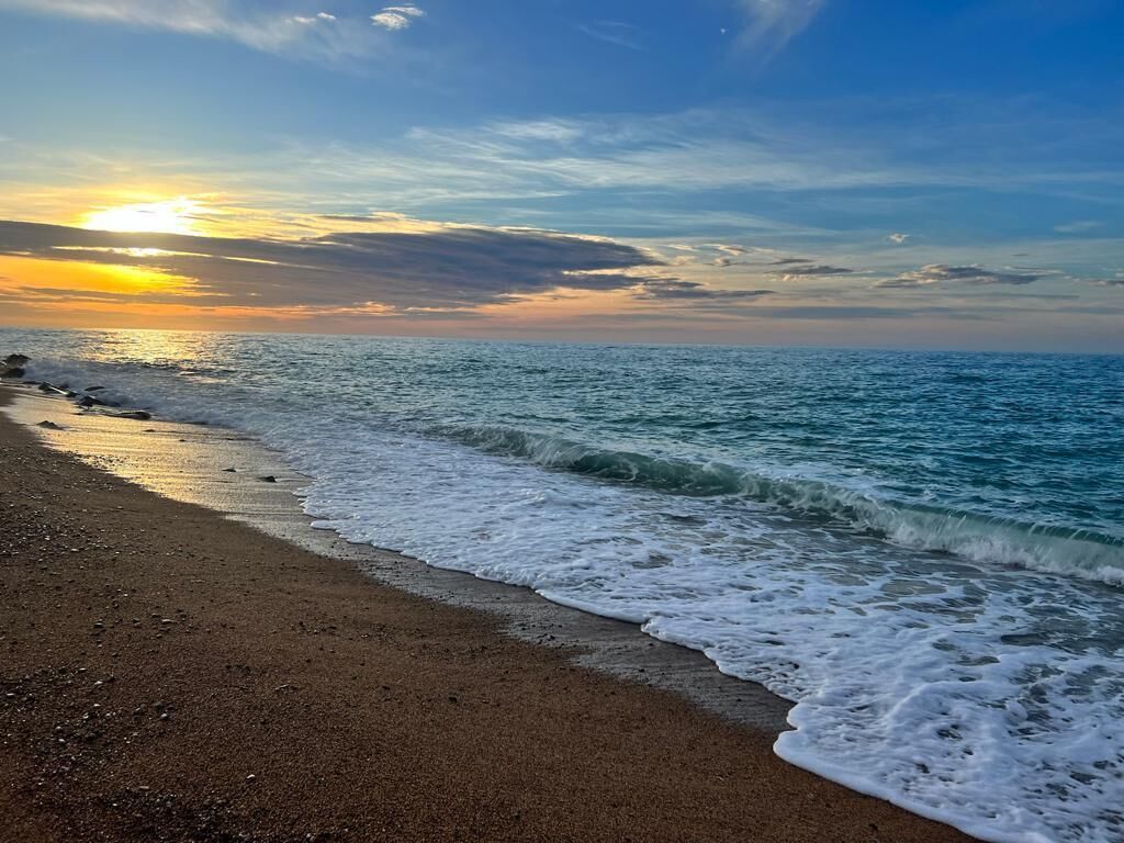 Een strand met golven die zachtjes op de kust komen, onder een zonsondergang.