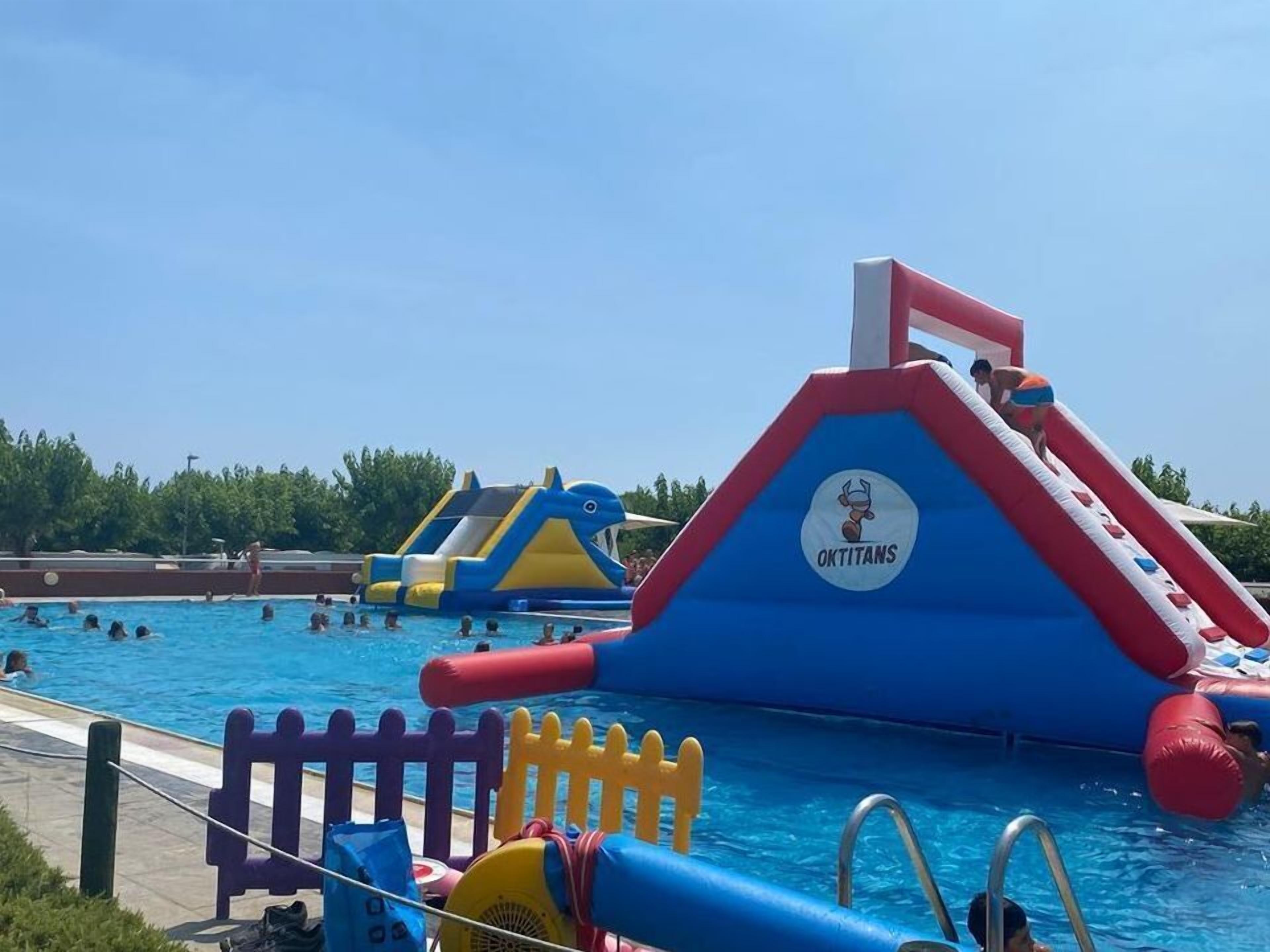 A swimming pool with inflatable slides and a fence.