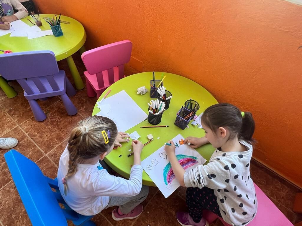 Two children drawing at a table with art supplies.
