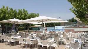 Outdoor seating with umbrellas, a pool, and a clear sky.