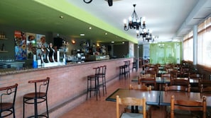 A restaurant with a bar area, multiple tables and chairs, and a brick counter.
