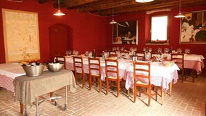 Zona pranzo con pareti rosse, travi in legno a soffitto e tovaglie a quadri. Sulla tavola, secchielli di metallo con bottiglie, e il pavimento è piastrellato.