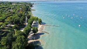 An aerial view of a coastal area with a clear beach, dense greenery, and a calm sea.