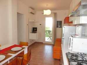 A compact kitchen with a gas stove, a coffee maker, and a dining area with a table and chairs. - Modern Flat With Swimming Pool and Solarium (San Michele al Tagliamento)