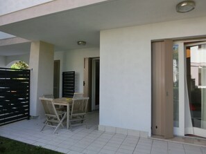 A covered patio area with a table and chairs, a sliding glass door, and a black gate. - Modern Flat With Swimming Pool and Solarium (San Michele al Tagliamento)