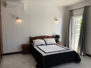 A bedroom with a bed, bedside lamps, a nightstand, a wall-mounted air conditioner, and a window with curtains.