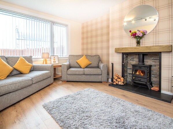 A living room with two grey sofas, a fireplace, and a large mirror on the wall. - 4 bedroom accommodation in Brora (Brora)