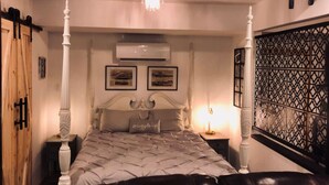 A four-poster bed with a tufted bedspread, a bedside table with a lamp, and a decorative wall panel. - French Cottage Studio • Dog-Friendly • Near Amelia Island (Fernandina Beach)