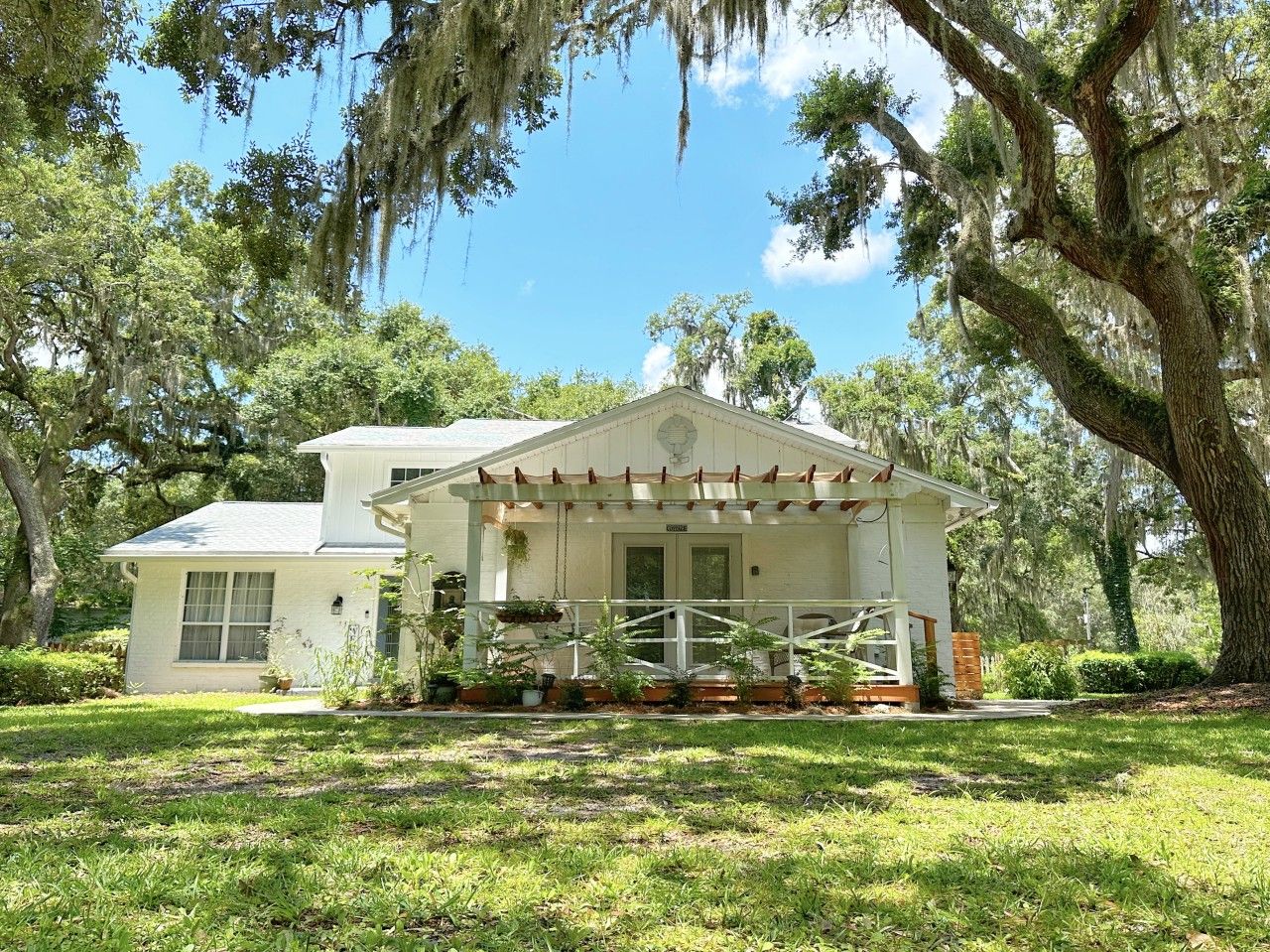 A two-story house with a porch, surrounded by trees and greenery.